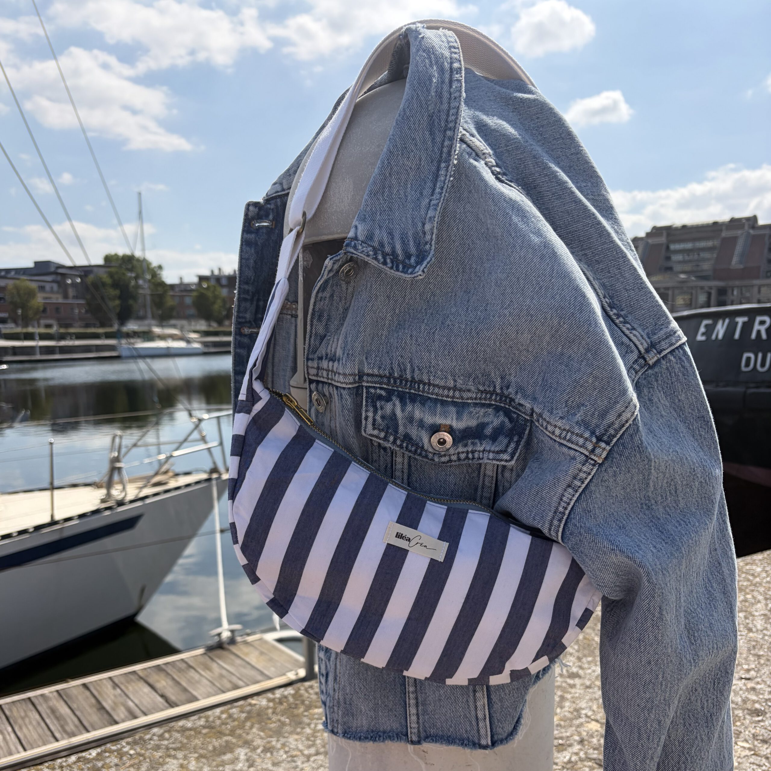 sac marcelle modele marin 1 sac demi lune marcelle modèle marin accroché sur une borne avec une veste en jean en bord de mer